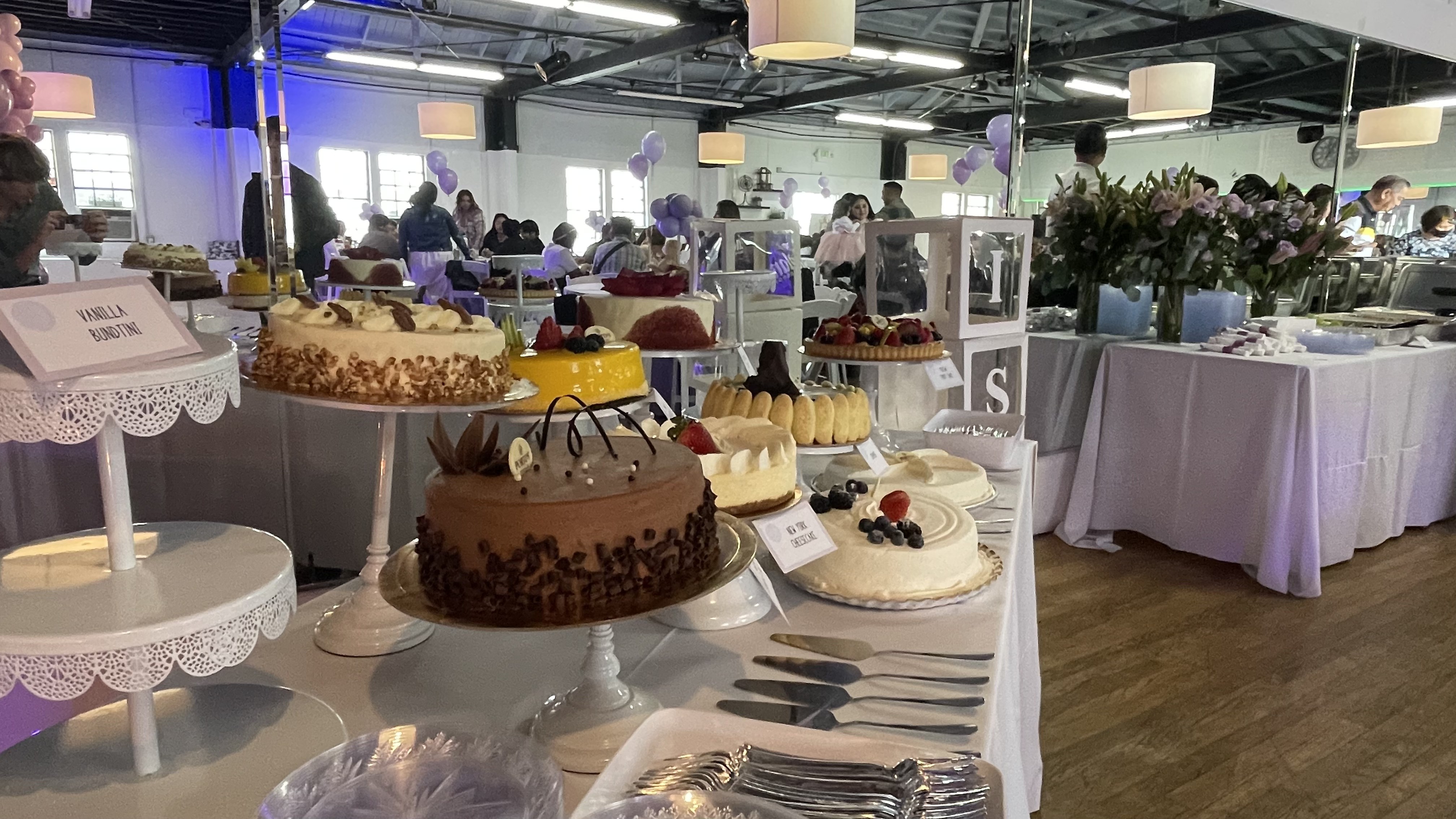 Dessert table with assorted cakes on white pedestals under pendant lights