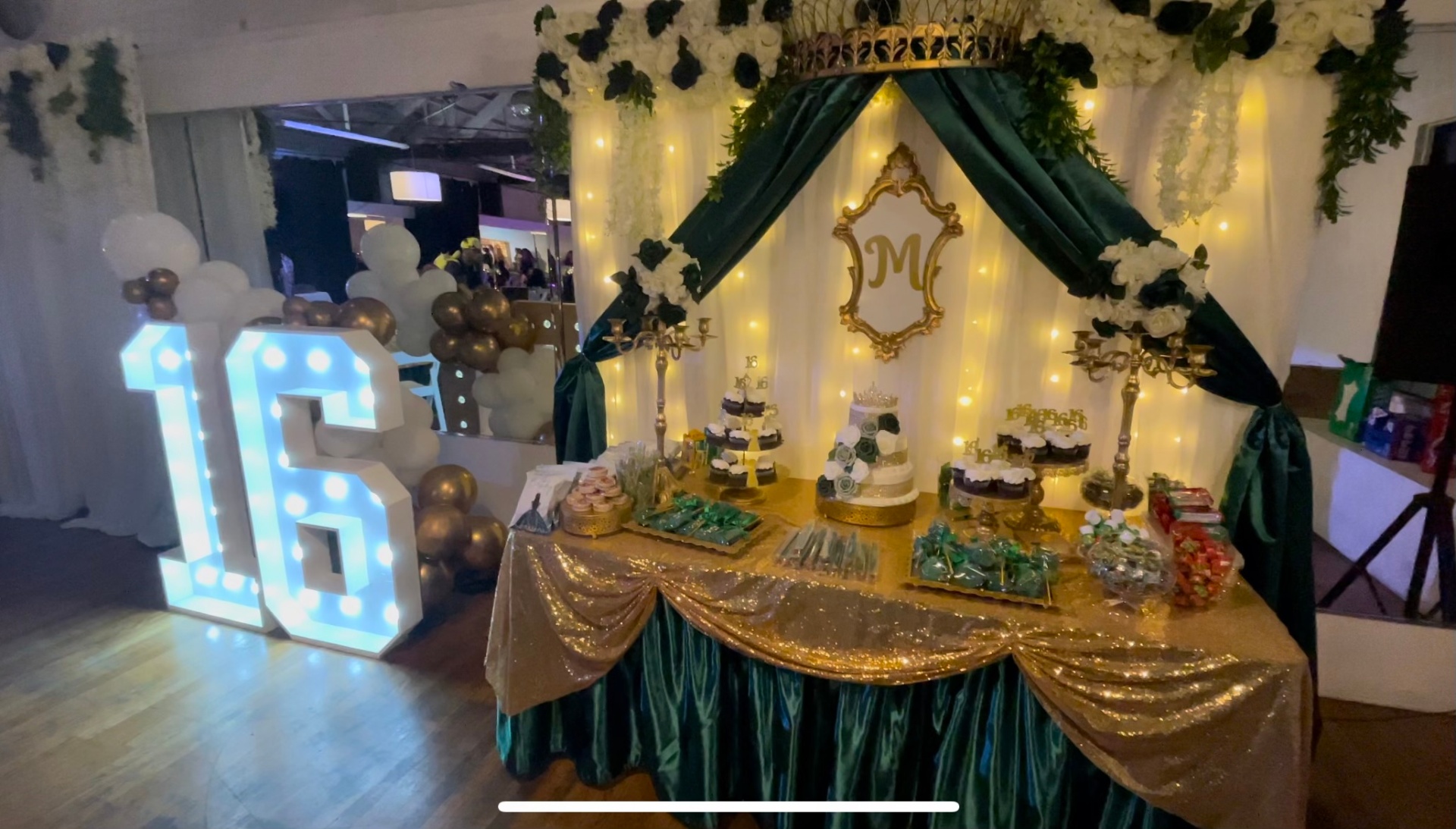 Sweet sixteen dessert display with floral backdrop and green drape